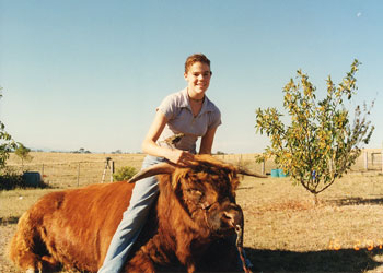 Girl with small bird on her hand sitting on the back of a Highland Bull